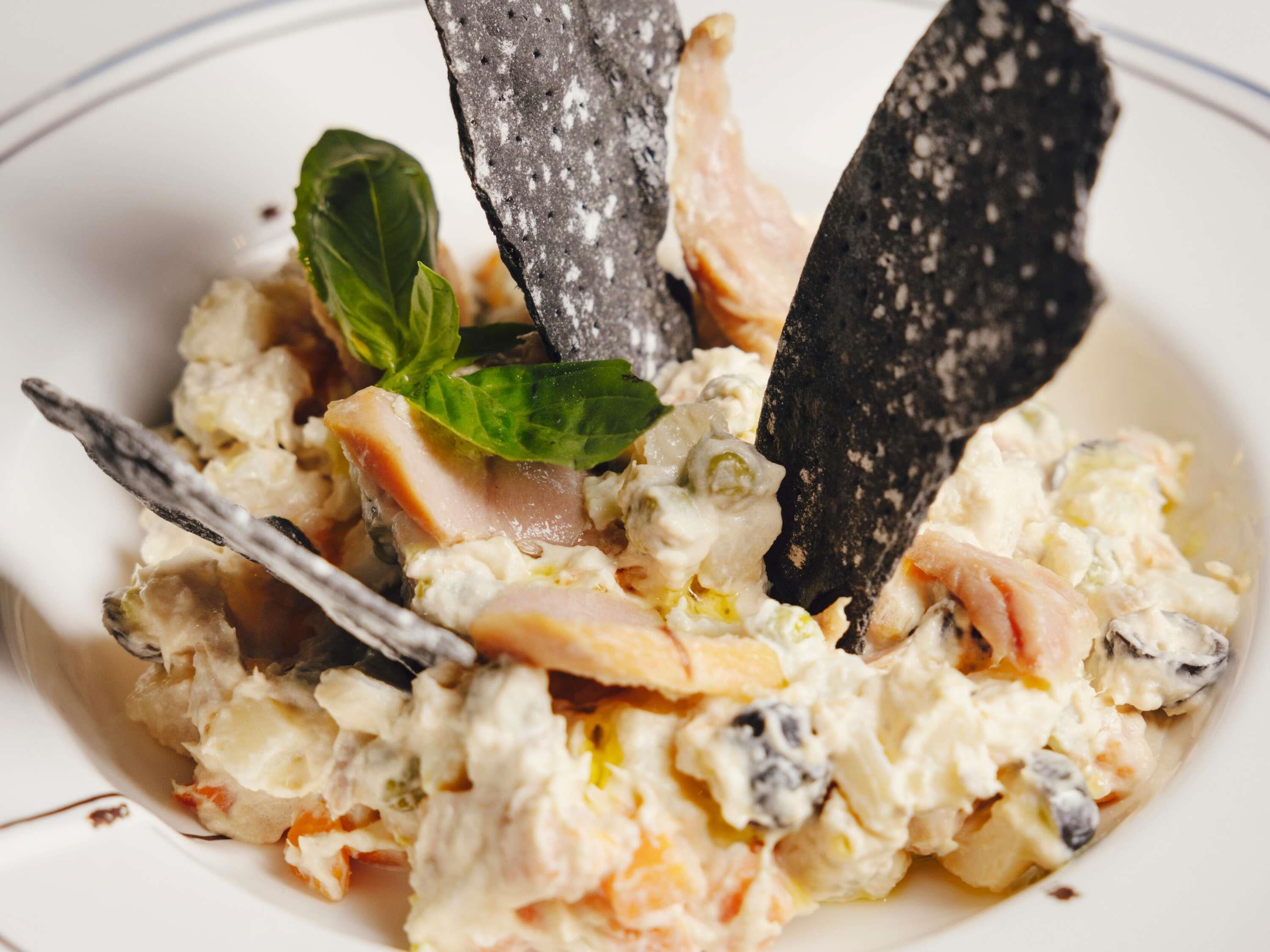 A dish with a creamy texture, garnished with a green leaf and two dark, speckled items.