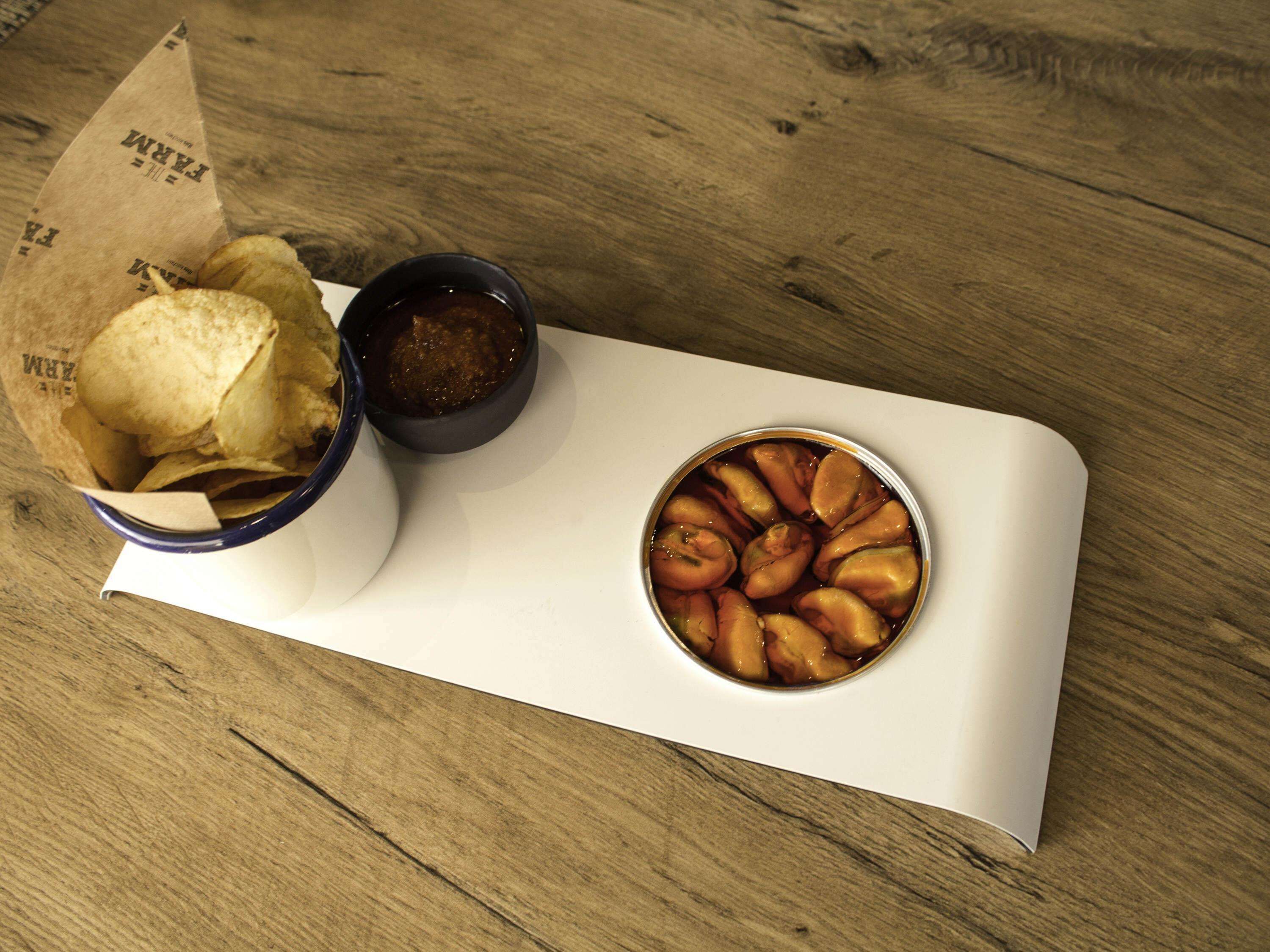 Una mesa de madera con una bandeja blanca que sostiene un bol de fruta, un recipiente pequeño de salsa y una bolsa de papel con papas fritas.