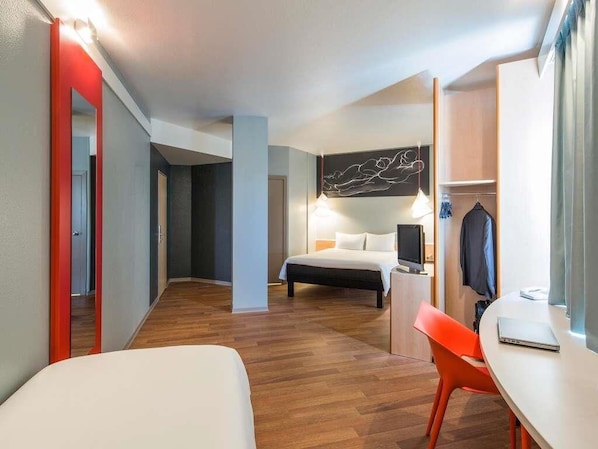 A hotel room with a bed, a desk with a chair, a TV, and a wardrobe.
