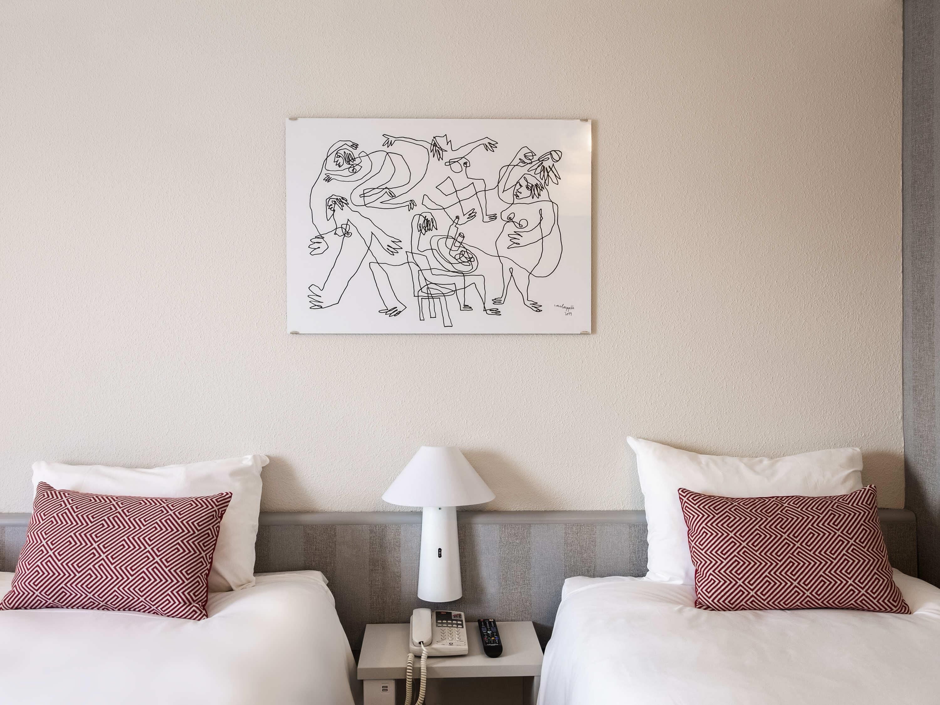 Une chambre d’hôtel avec deux lits, une table de chevet avec une lampe, une télécommande et une œuvre d’art accrochée au mur.