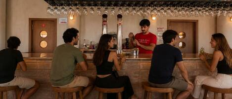 A bar area with stools, a bartender, and a variety of bottles and glasses on shelves.