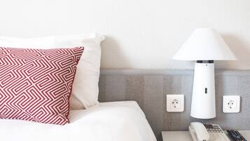 Una habitación de hotel con una cama, un cojín estampado, una lámpara blanca, un teléfono y un control remoto sobre una mesita de noche.