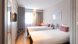 Habitación de hotel con dos camas, un televisor montado en la pared, un escritorio con una silla y una ventana con cortinas.