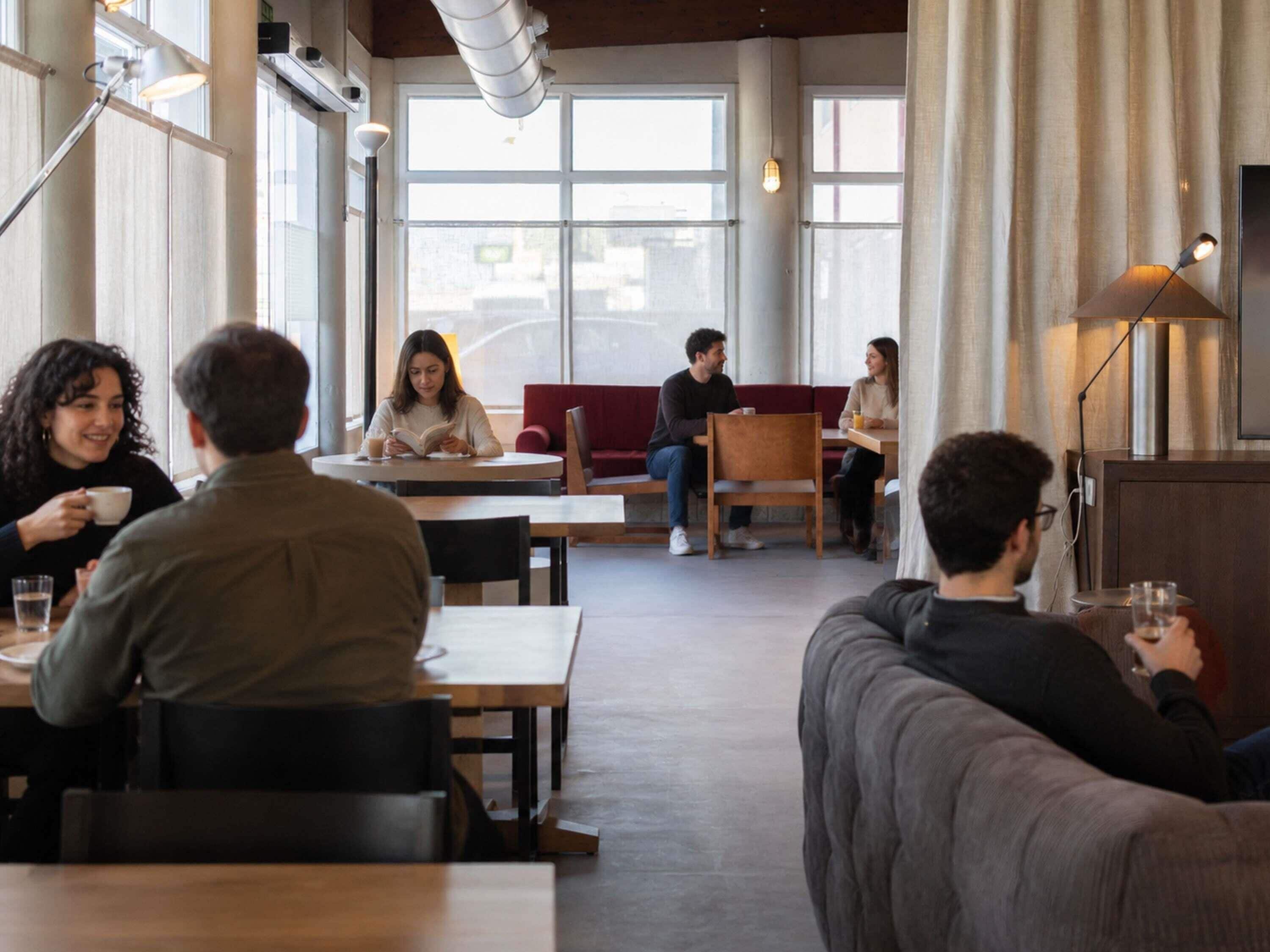 Una cafetería moderna con amplios ventanales, mesas de madera y una variedad de opciones de asientos, incluyendo sillas y sofás.