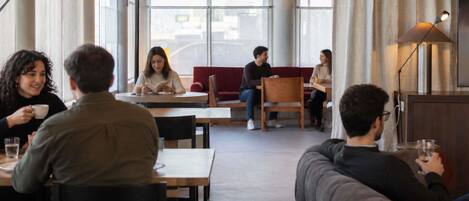 Una cafetería moderna con amplios ventanales, mesas de madera y una variedad de opciones de asientos, incluyendo sillas y sofás.