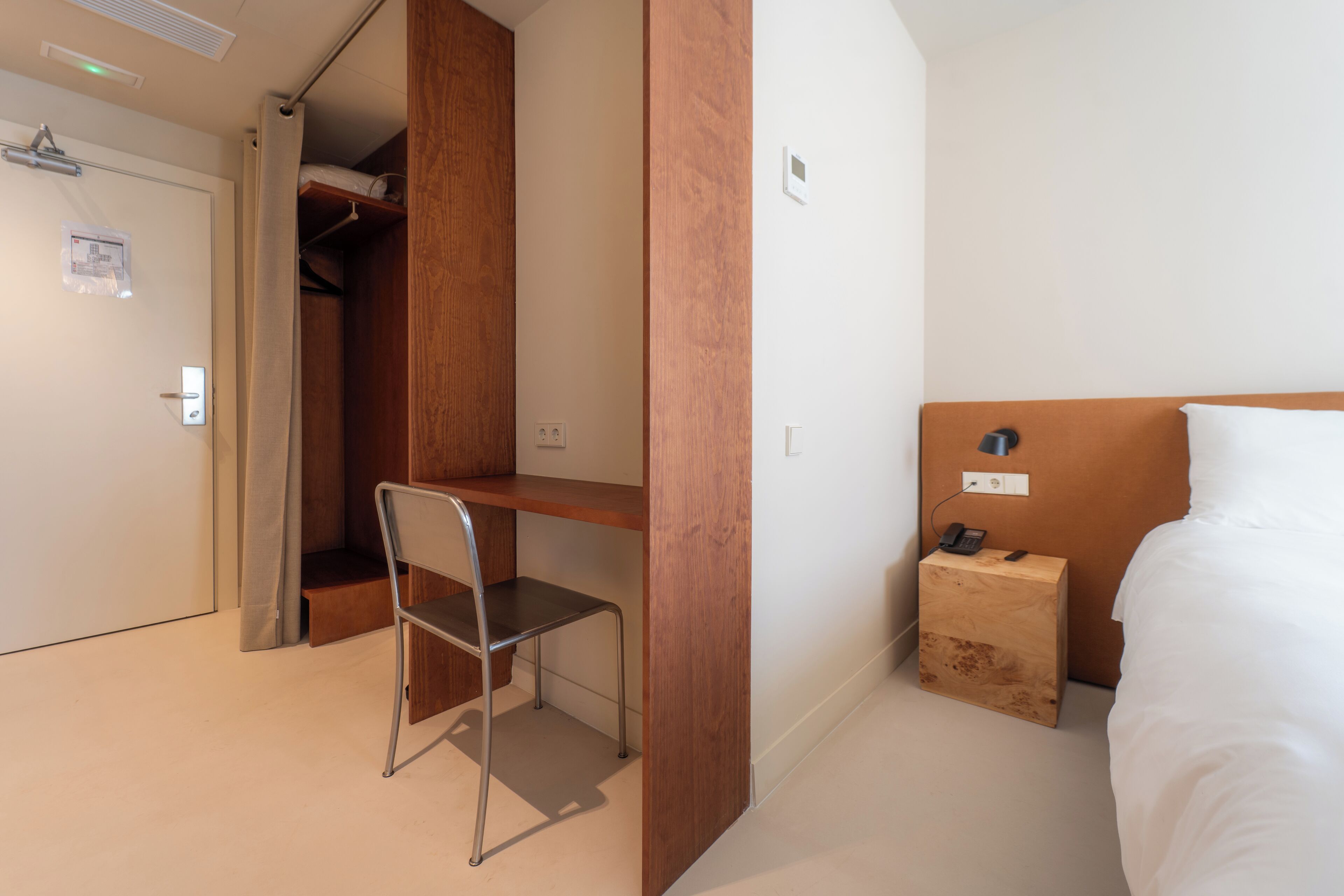 Ein Hotelzimmer mit einem Bett, einem Schreibtisch mit Stuhl, einem Holzschrank und einem Nachttisch mit Telefon.