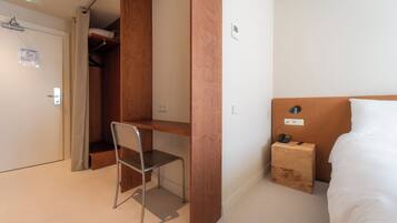 Habitación de hotel con cama, escritorio con silla, armario de madera y mesita de noche con teléfono.