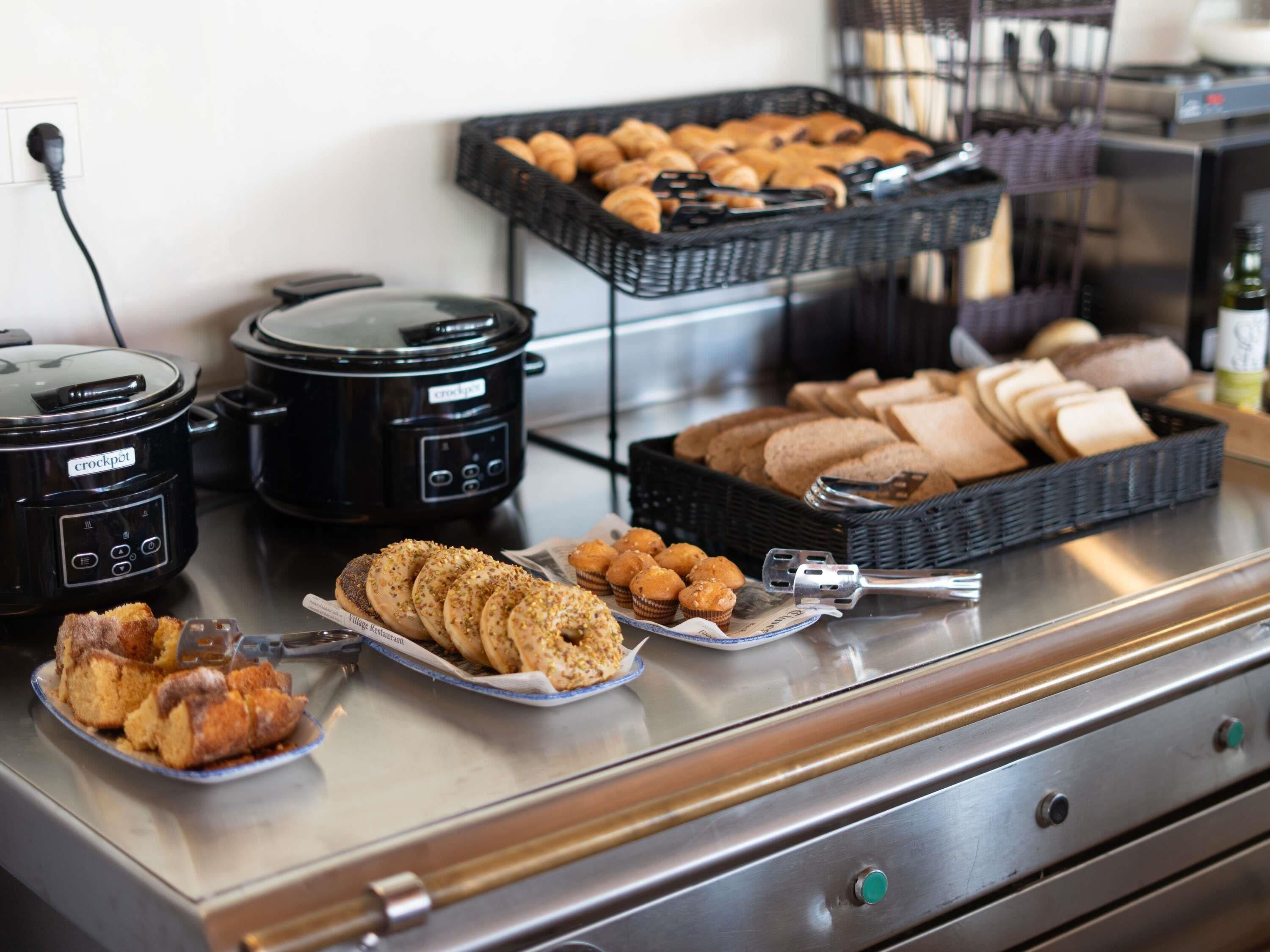 A buffet with various baked goods, including bread, muffins, and pastries, and two slow cookers.