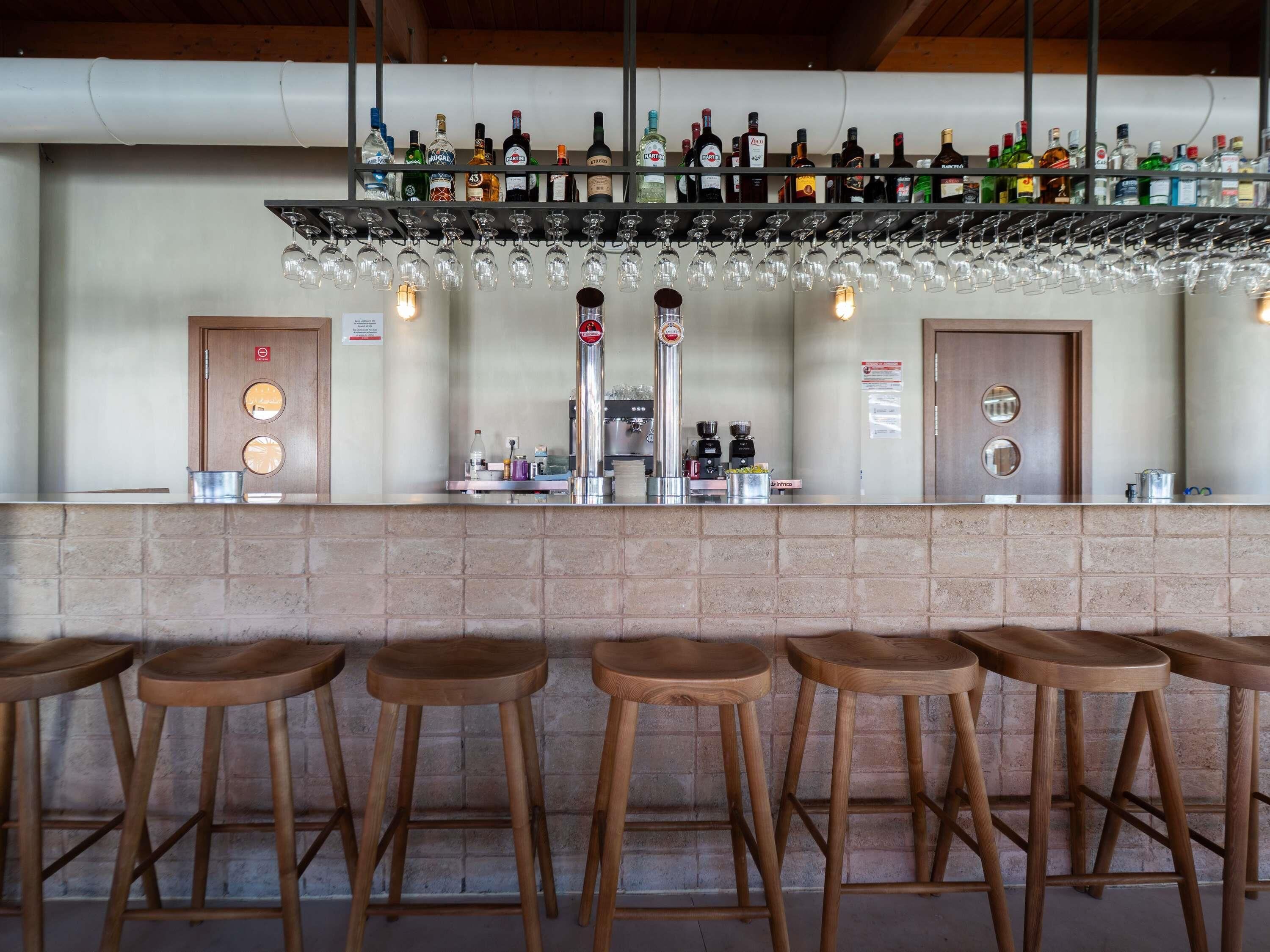 A bar area with a brick counter, multiple stools, a variety of liquor bottles, and a coffee machine.