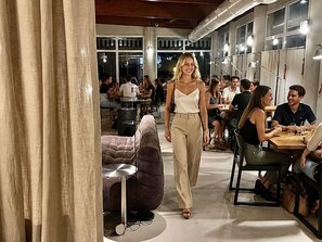An indoor space with tables and chairs, a sofa, and a person walking. - ibis Valencia Alfafar (Alfafar)