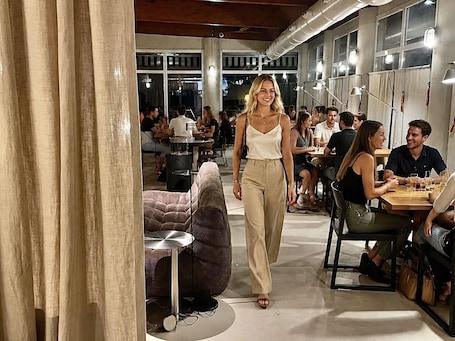 An indoor space with tables and chairs, a sofa, and a person walking.. ibis Valencia Alfafar