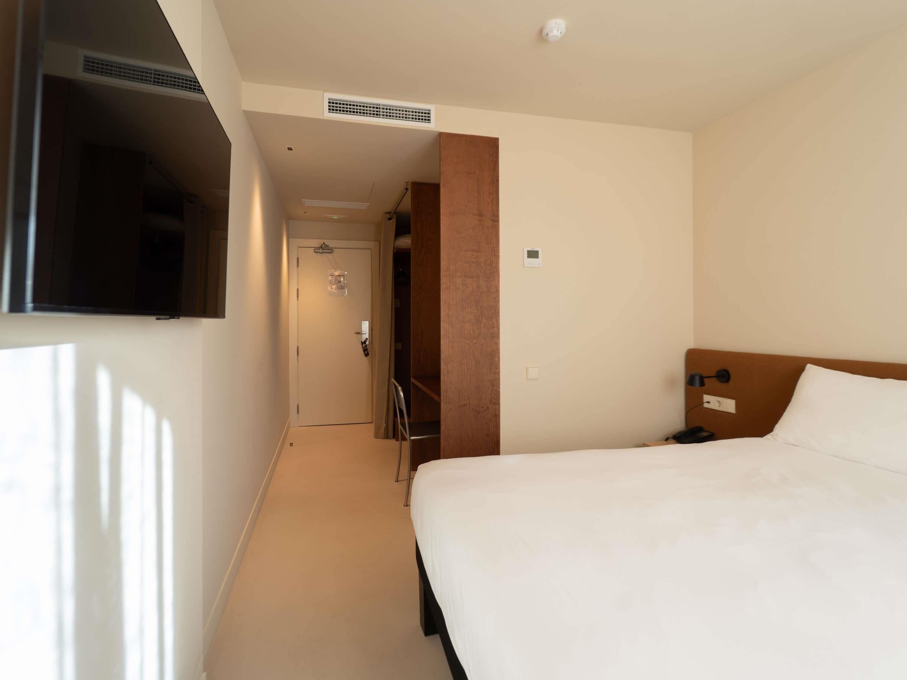 Ein Hotelzimmer mit Bett, Wandfernseher, einer Tür mit Griff und Lichtschalter.