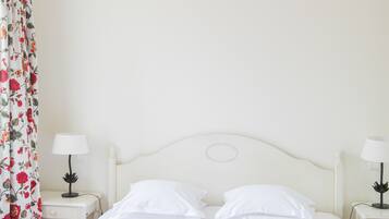 Un lit bien fait, recouvert d’une couvre-lit à motifs floraux, deux tables de chevet avec des lampes et un rideau à fleurs.