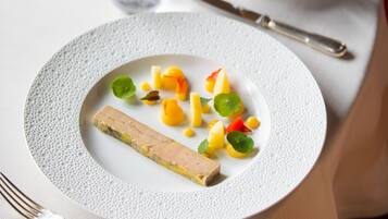 Une table à manger avec une assiette de nourriture, une fourchette, un couteau et un verre de vin blanc.