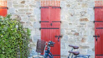 A stone building with red shutters and a bicycle parked in front.