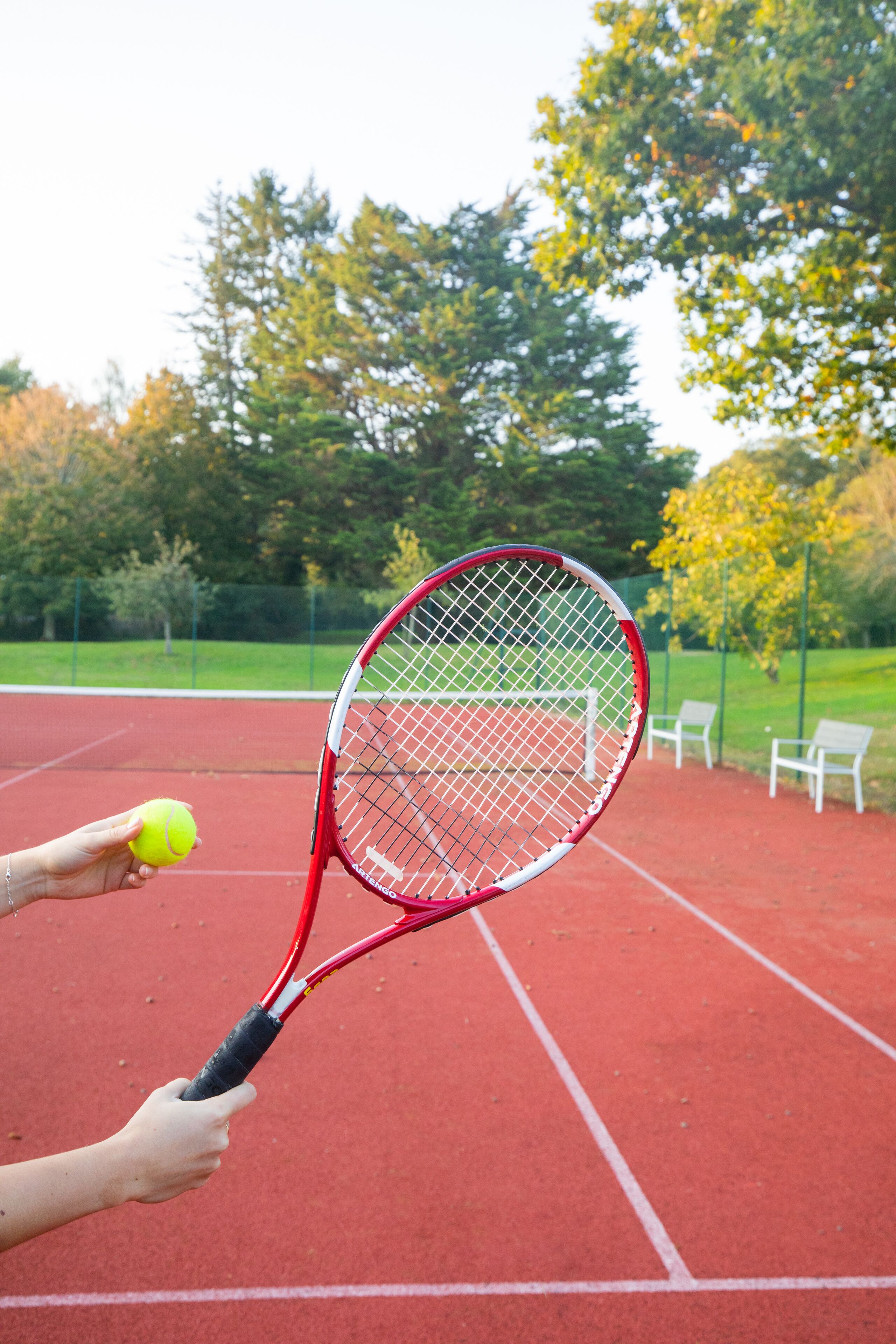 Una cancha de tenis con superficie roja, una raqueta de tenis y una pelota.
