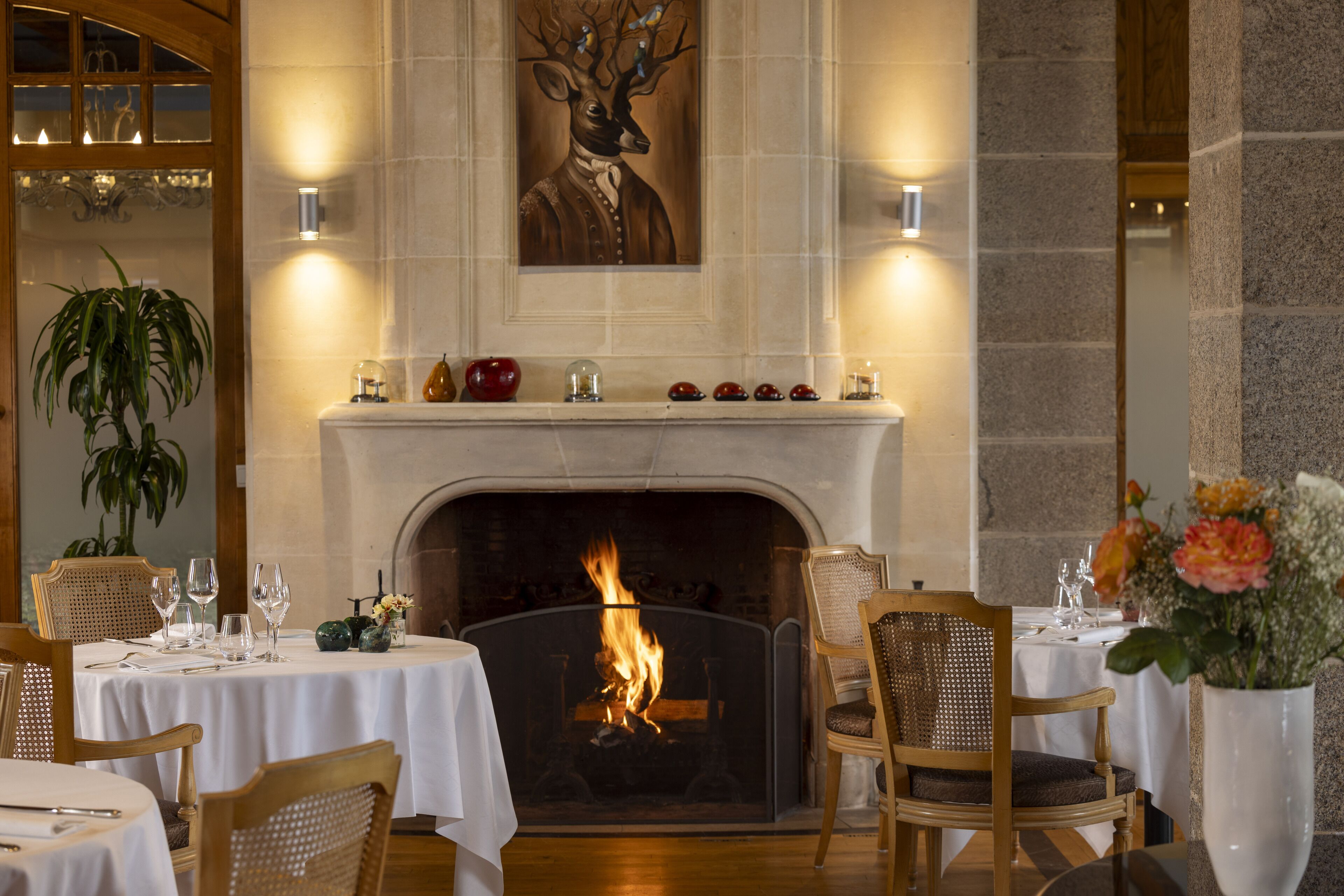 A dining area with a fireplace, white tablecloths, and wooden chairs.