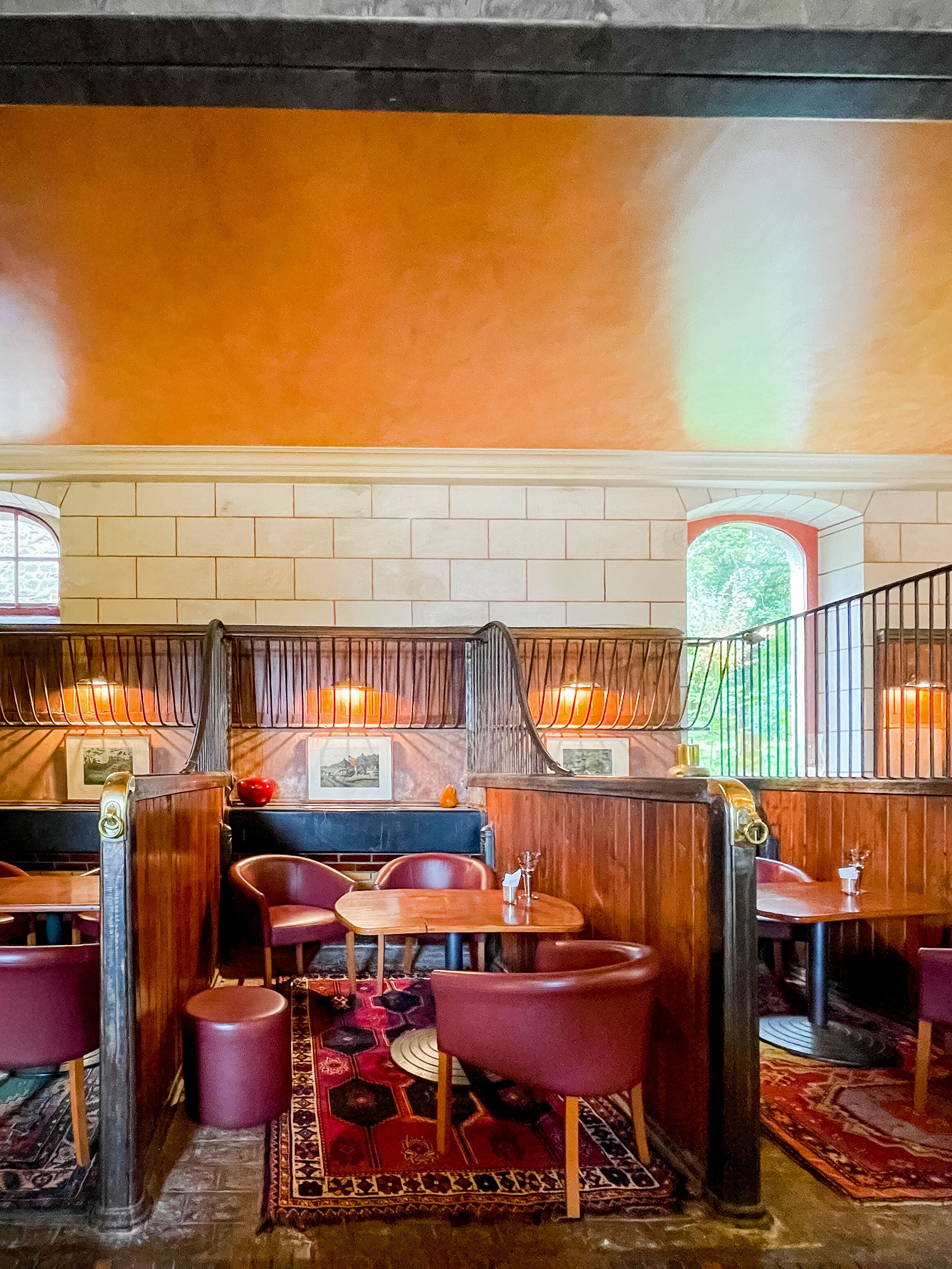 A restaurant interior with booths, red upholstered chairs, patterned rugs, and brick walls.