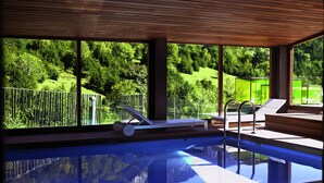 Una piscina interior moderna con dos tumbonas y vistas a un paisaje verde exuberante.