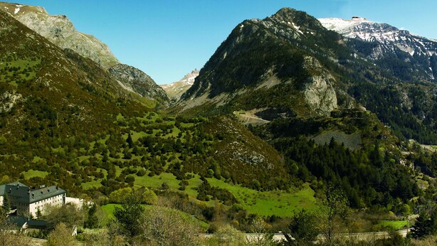 Un paisaje montañoso con un edificio grande rodeado de vegetación y un pico nevado al fondo.