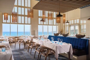 A restaurant with tables set for dining, large windows overlooking the sea, and a view of the ocean.