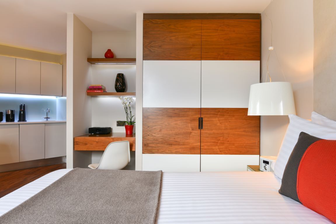 Ein modernes Hotelzimmer mit Bett, Nachttisch, Lampe und einem Holzschrank.