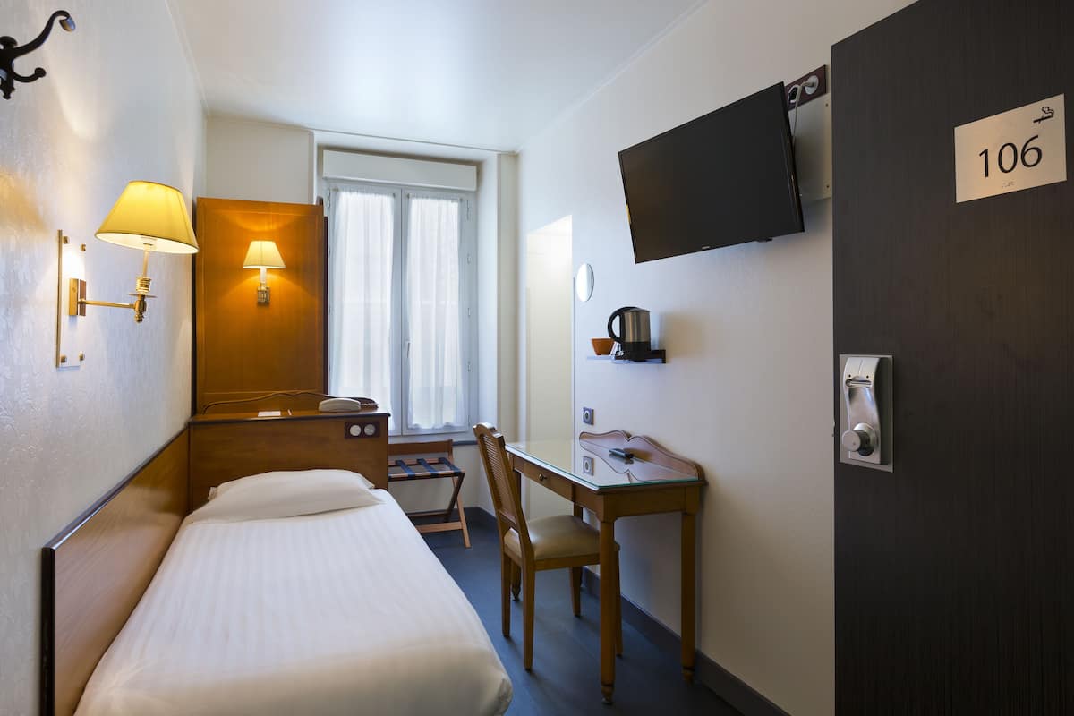 Habitación de hotel con cama, escritorio, silla, televisor, cafetera y puerta con el número 106.