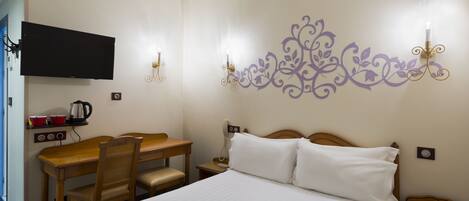 Habitación de hotel con cama, escritorio con silla, televisor montado en la pared y un elemento decorativo en la pared.