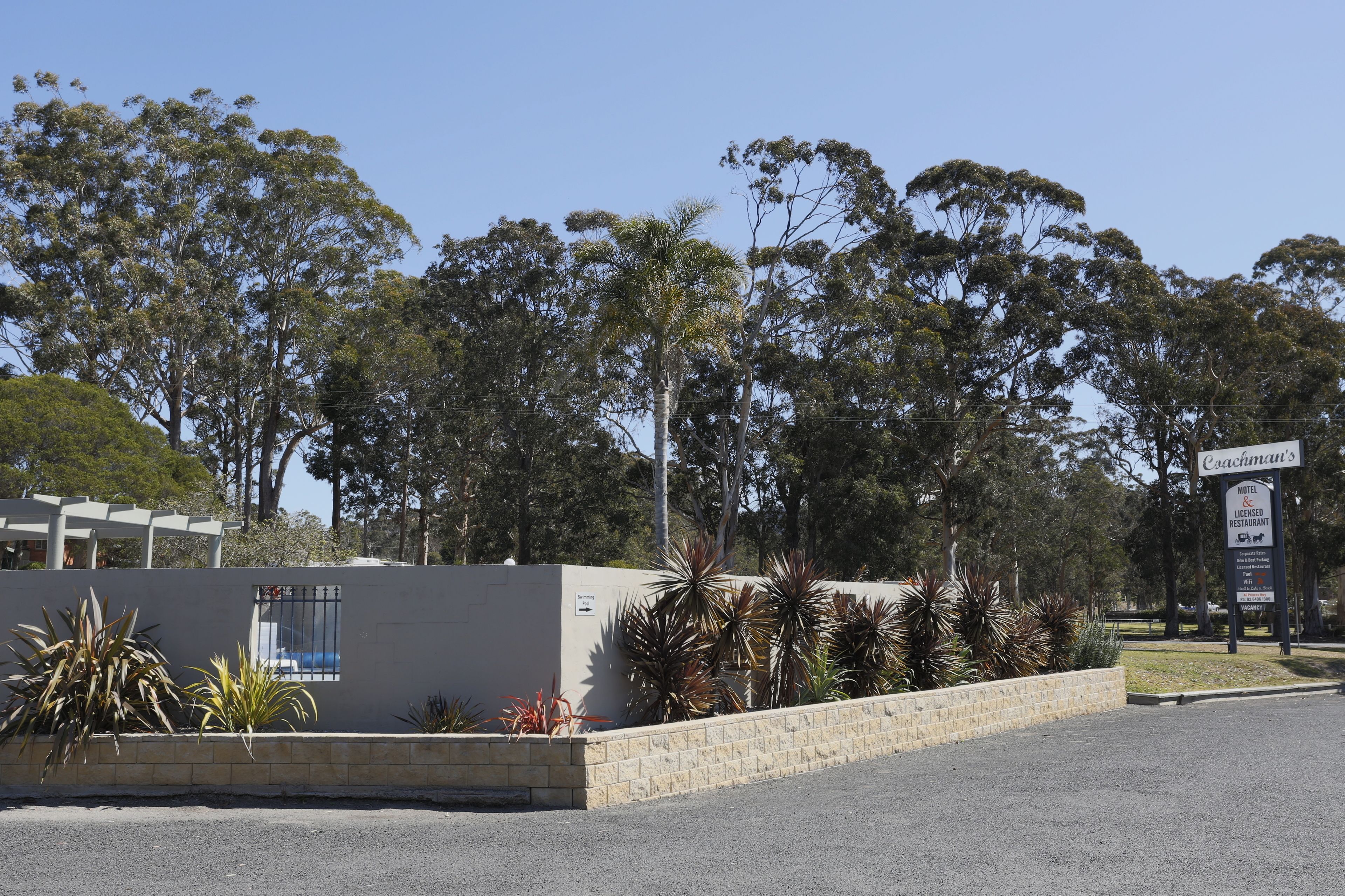 A hotel with a signboard, a paved area, and a row of trees in the background.