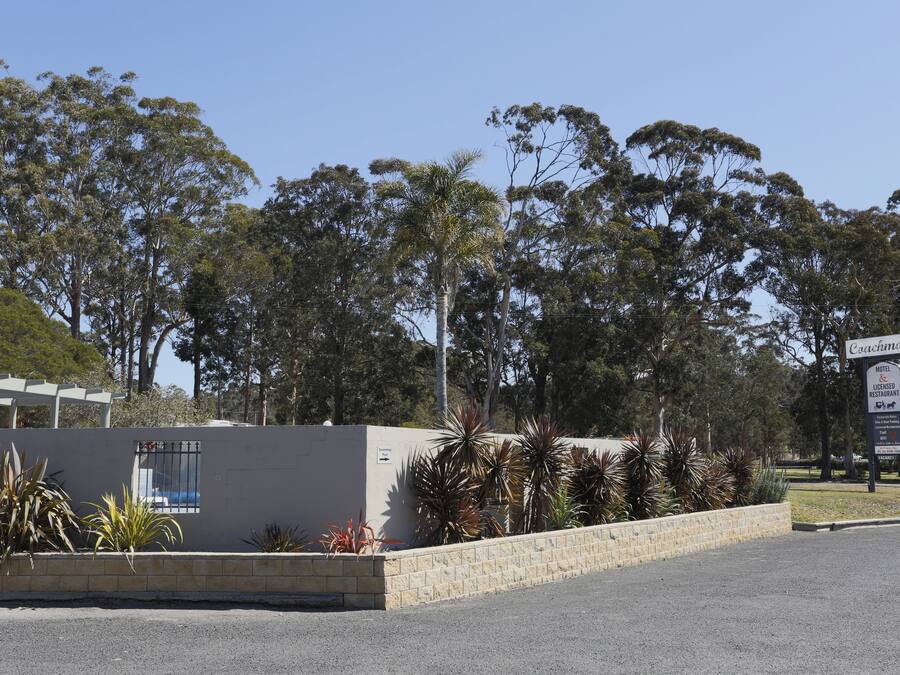 A hotel with a signboard, a paved area, and a row of trees in the background.