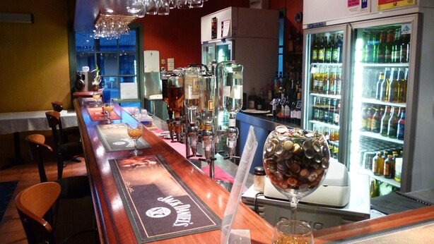 Een bar met een lange toonbank, barstoelen, diverse flessen en glazen, en een koelkast vol met drank.