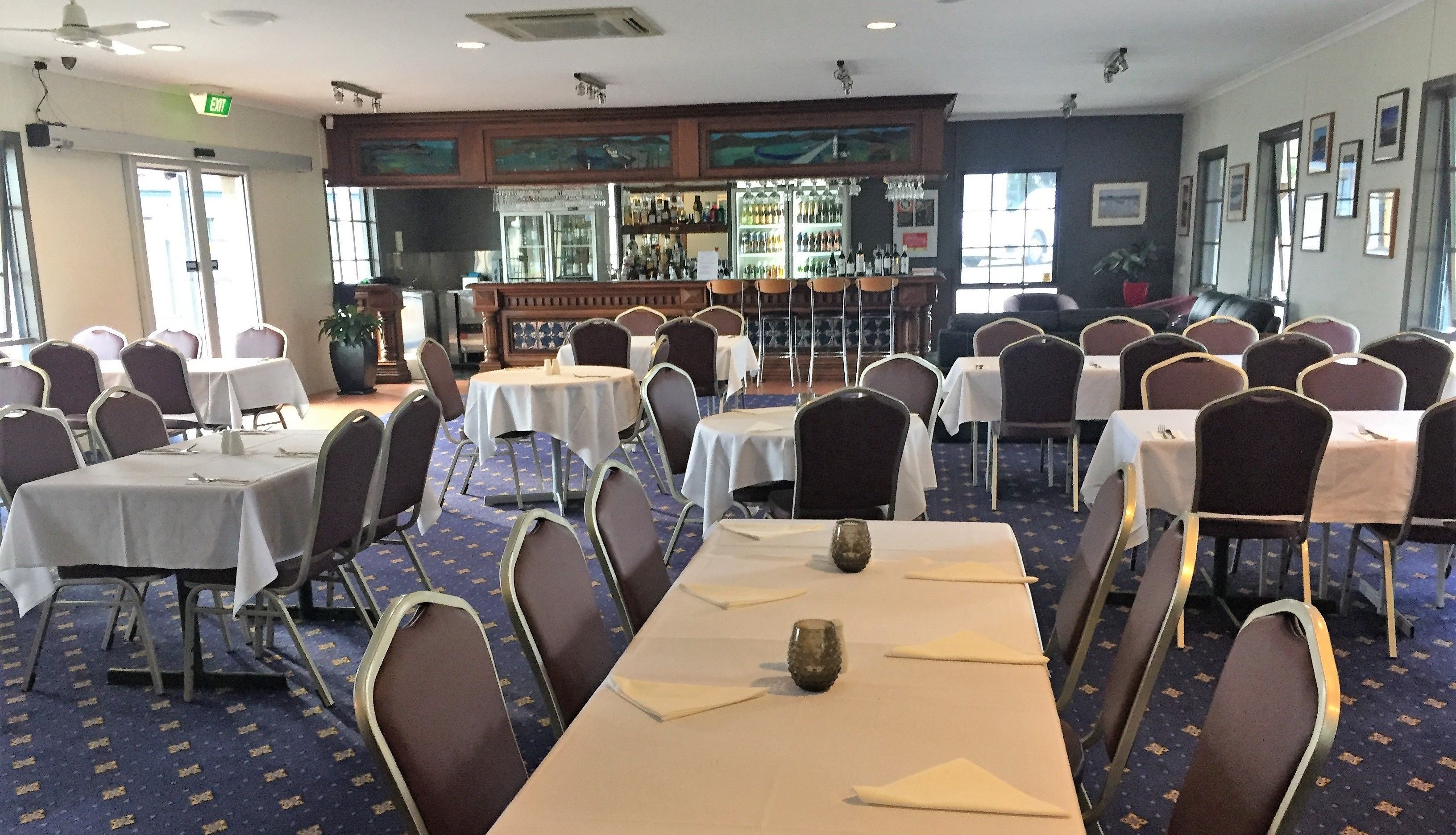 Un salón de conferencias con varias mesas y sillas, una zona de bar con diferentes botellas, y cuadros en las paredes.