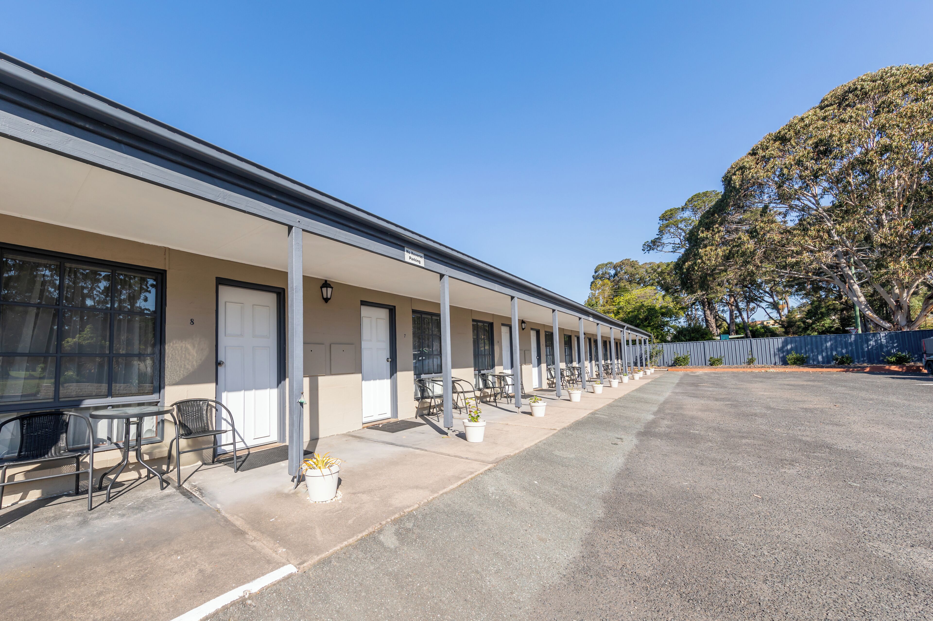 Un motel avec une série de chambres, des places assises à l’extérieur et un parking.
