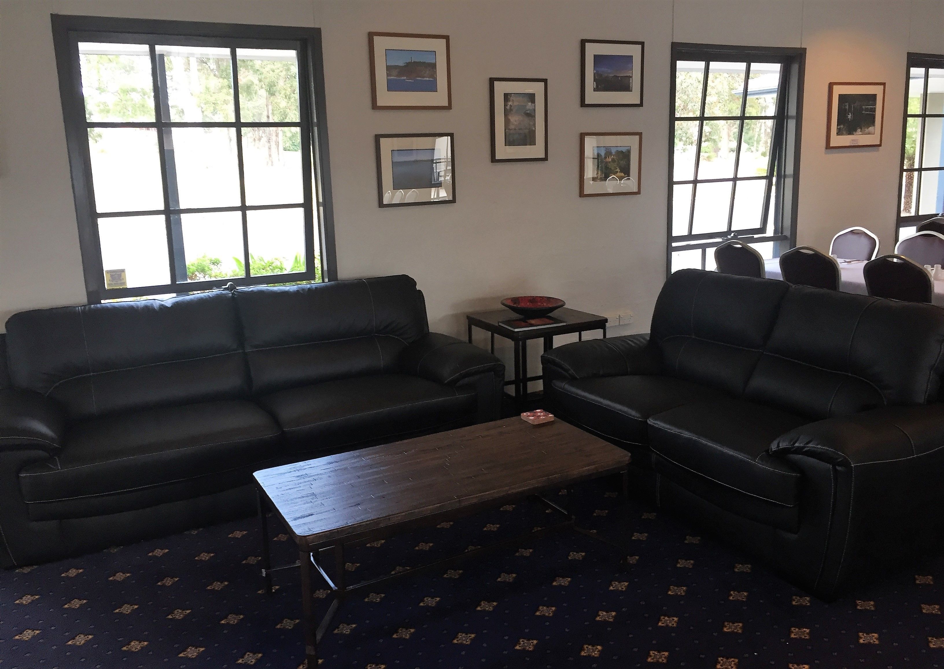 A living room with two black leather sofas, a wooden coffee table, and a patterned carpet.
