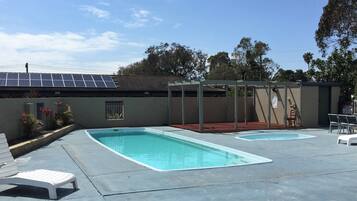 A swimming pool area with two pools, lounge chairs, and a pergola structure.