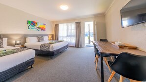 Een hotelkamer met twee bedden, een eettafel, een televisie en een schilderij aan de muur.