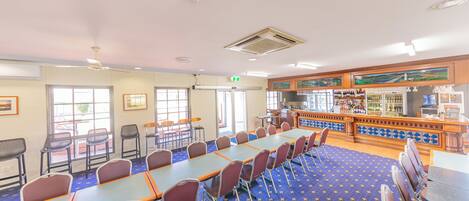 A conference room with tables and chairs, a bar area with shelves of bottles, and a patterned carpet.