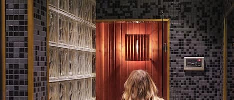A person in a white robe walking through a hallway with tiled walls and a wooden door.