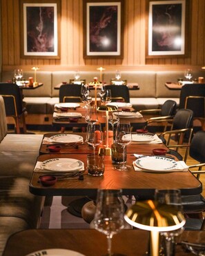Un restaurant avec une longue table à manger dressée pour le repas, entourée de banquettes et de chaises.