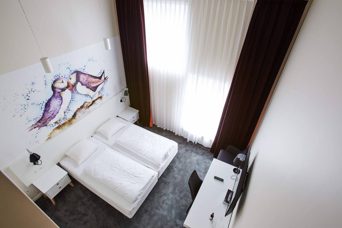 Une chambre d’hôtel comprenant un lit, un bureau, une chaise, une table de chevet et une œuvre d’art fixée au mur représentant deux hiboux.