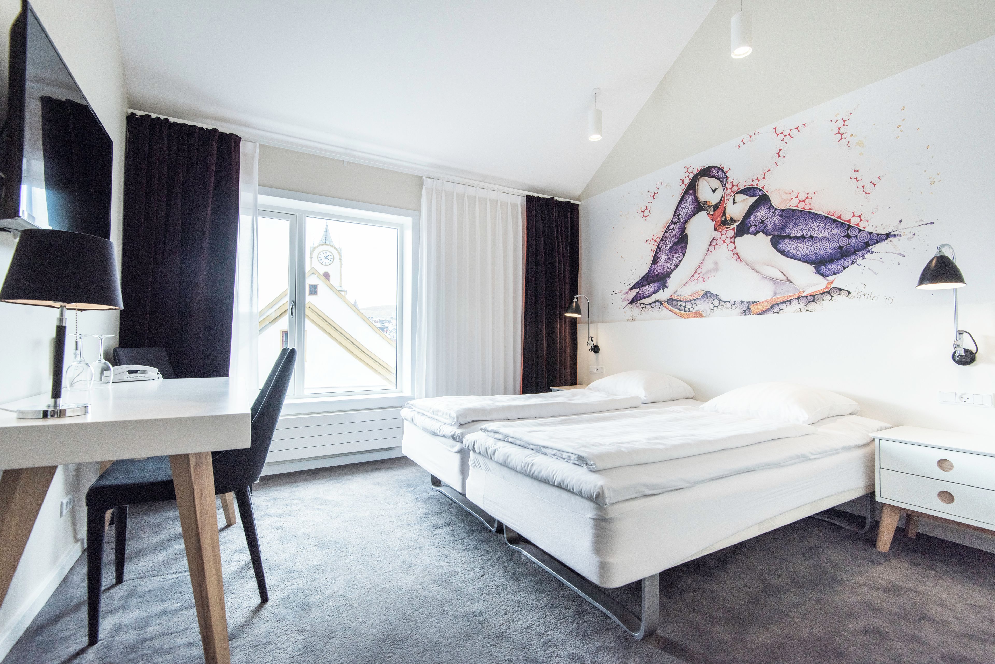 Quarto de hotel moderno com cama, escrivaninha, cadeira e uma janela grande.