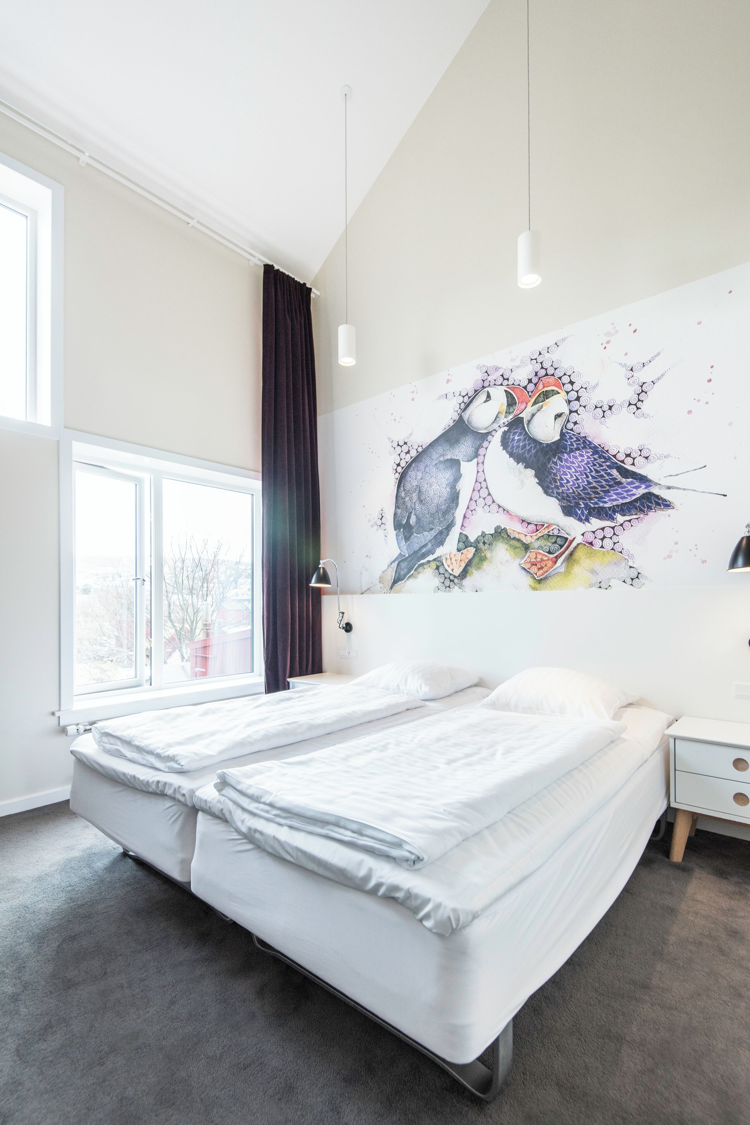 A modern bedroom with a large bed, a window, and a wall mural.