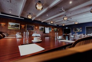 Un salón de conferencias con una larga mesa de madera, numerosas sillas y obras enmarcadas en las paredes.