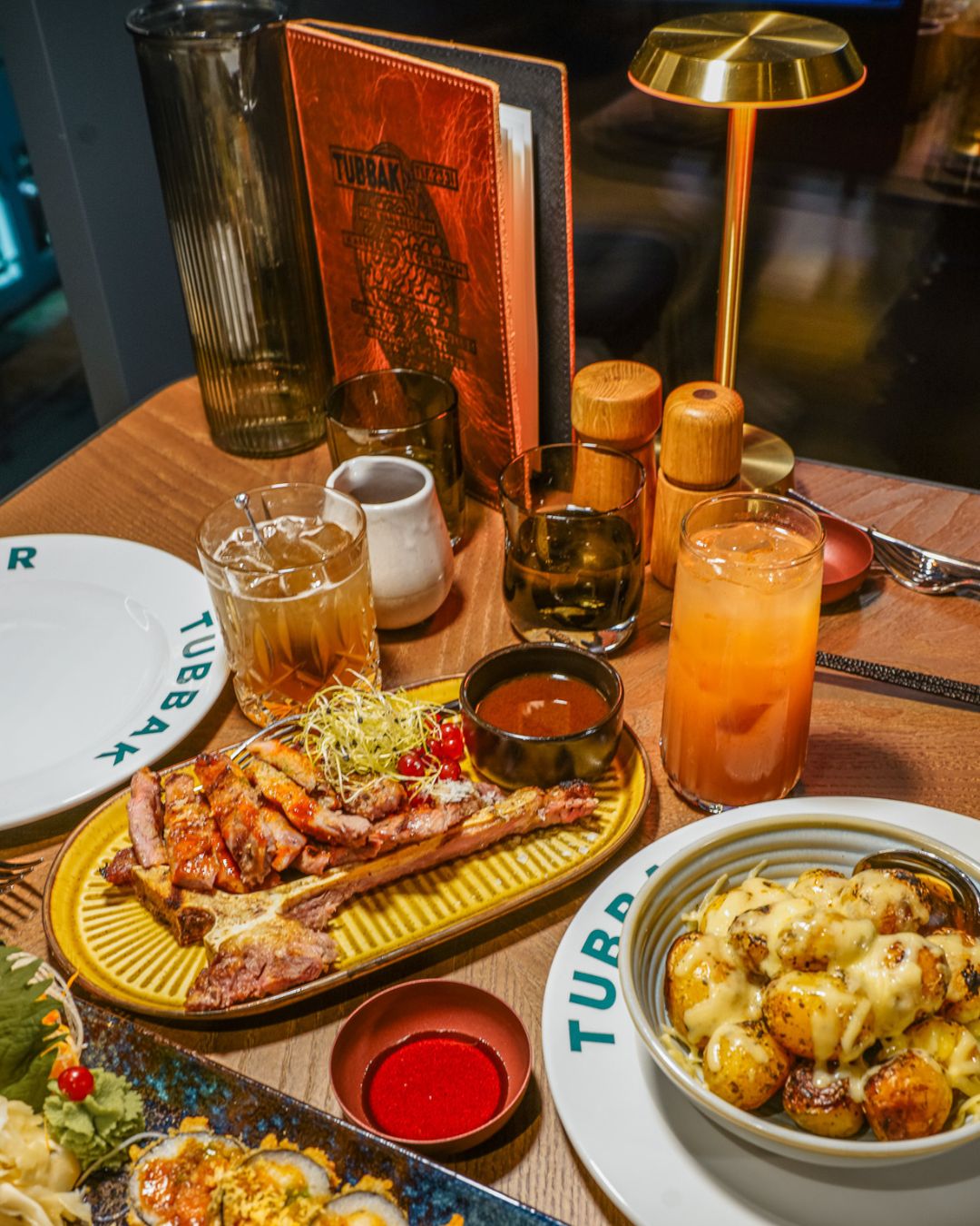Una mesa servida con diversos platos, bebidas y aderezos, lo que sugiere una experiencia gastronómica.