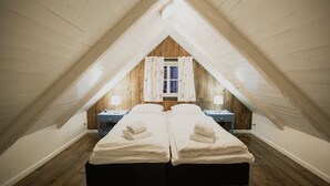 A room with two beds, wooden floors, a window with curtains, and bedside lamps.
