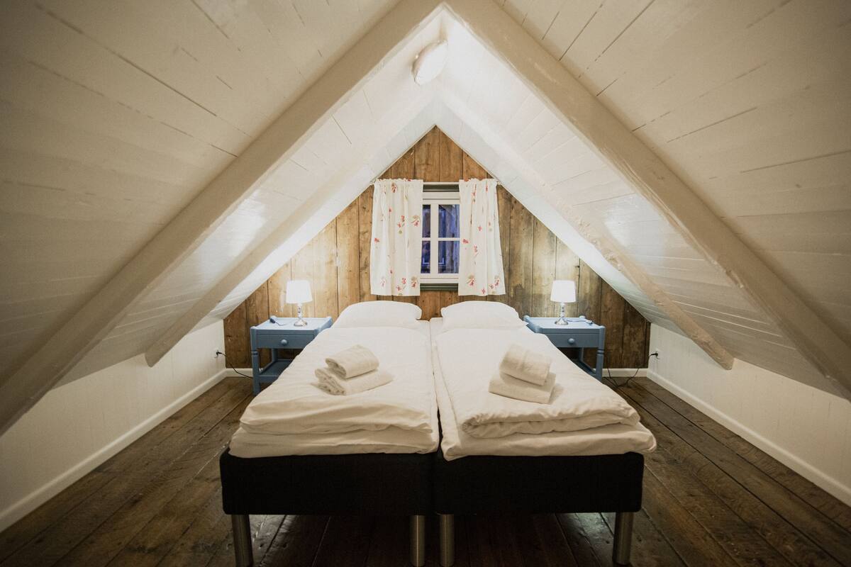 Une chambre avec deux lits, un plancher en bois, une fenêtre avec des rideaux et des lampes de chevet.