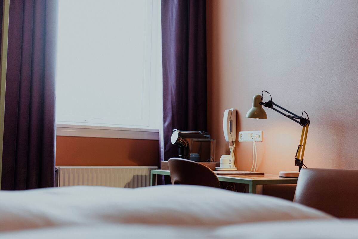 Une chambre d’hôtel avec un lit, un bureau doté d’une lampe, une tasse et une prise électrique.