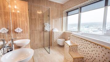 Ein modernes Badezimmer mit einem großen, ovalen Waschbecken, einer Duschkabine, einer Toilette und einem Fenster mit Blick auf die Stadt.