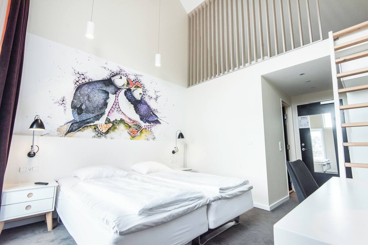 Une chambre moderne avec un grand lit, un bureau et une œuvre d’art accrochée au mur.