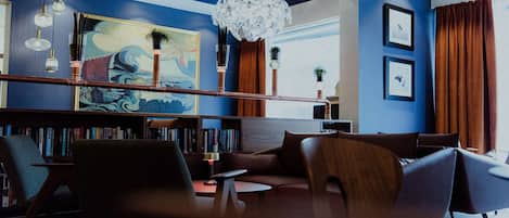A modern lounge area with a blue accent wall, a large abstract painting, a unique chandelier, and a bookshelf filled with books.